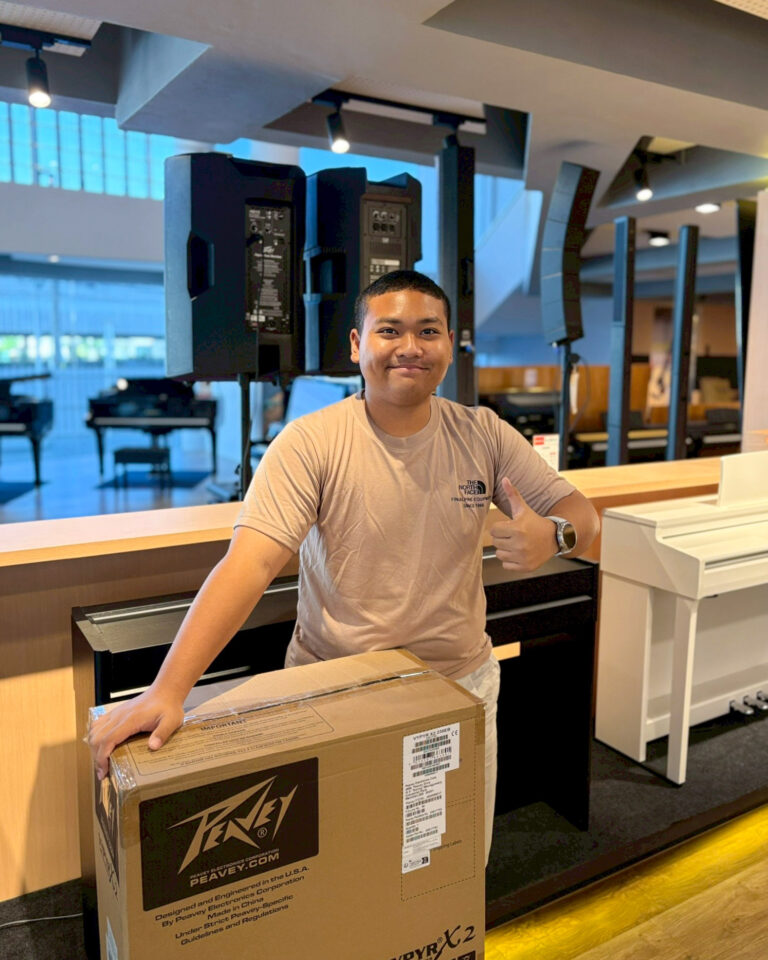 Smiling man at a checkout counter with a large boxed item labeled Peavey in front, giving a thumbs-up in a store.