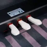 Close-up of three white piano pedals on a dark piano, with a warning label above the pedals. ขายราคาพิเศษ