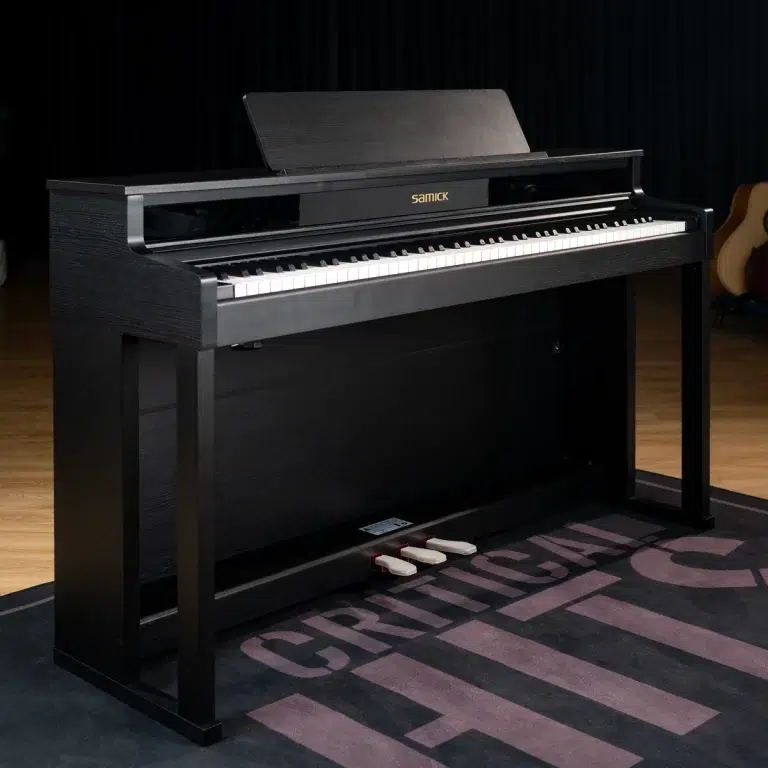 Black upright piano with three pedals on a dark rug in a music room; brand Samick visible on the fallboard. ขายราคาพิเศษ