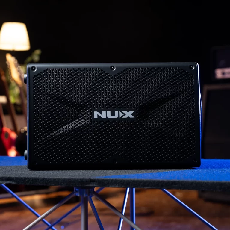 Front view of a black NUX speaker with a perforated grille on a blue surface in a dim room. ขายราคาพิเศษ