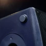 Close-up of a black volume knob on a dark blue speaker, with a vented grille visible to the right. ขายราคาพิเศษ