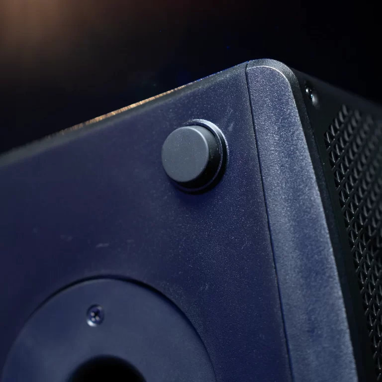 Close-up of a black volume knob on a dark blue speaker, with a vented grille visible to the right. ขายราคาพิเศษ
