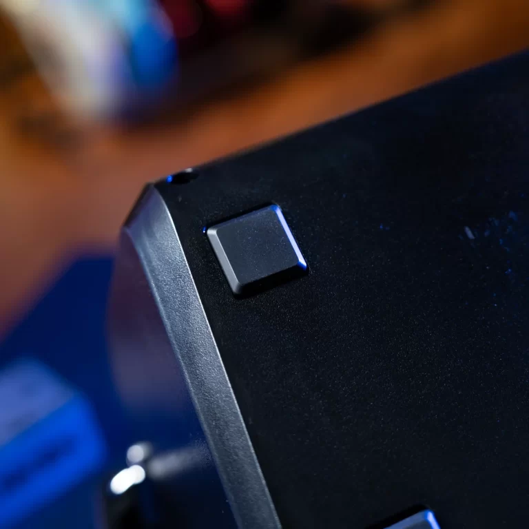 Close-up of a small square push button on a black electronic device, illuminated with blue lighting ขายราคาพิเศษ