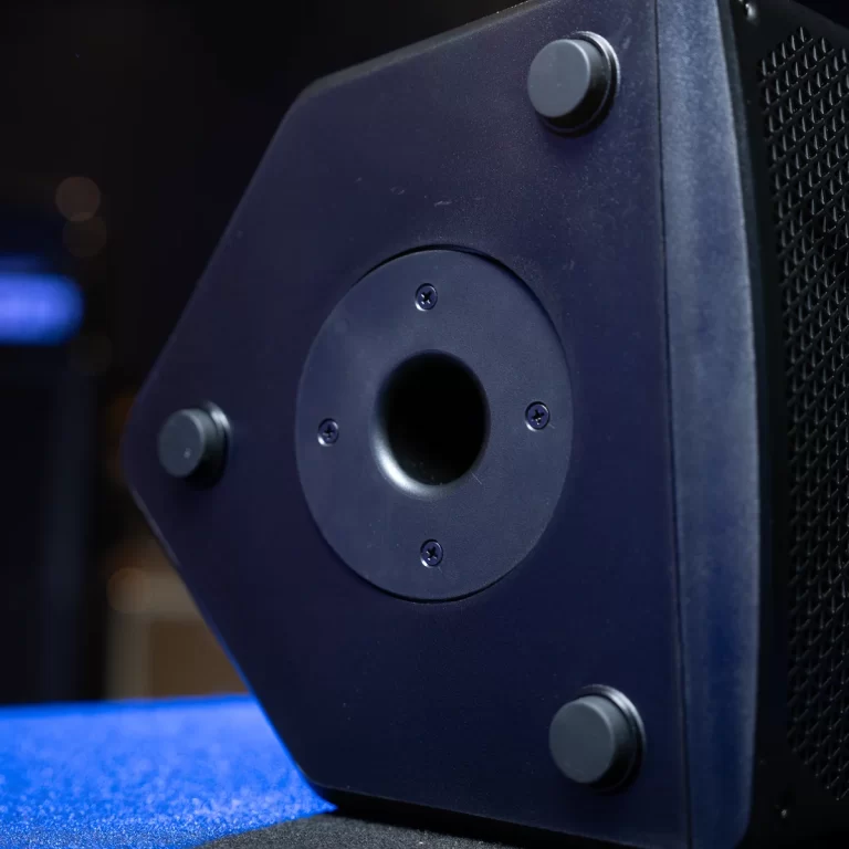 Close-up of a dark blue speaker cabinet with a circular port in the center, four screws around it, and rubber feet on a blue carpeted surface. ขายราคาพิเศษ