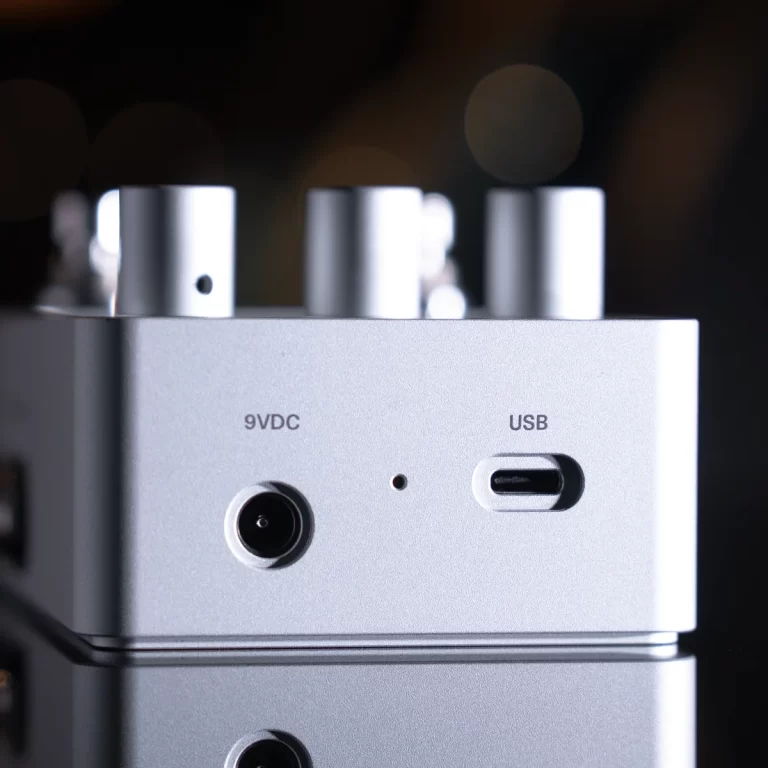 Close-up of a silver electronic device showing a 9V DC input and a USB-C port on the front panel, with metallic knobs in the blurred background. ขายราคาพิเศษ