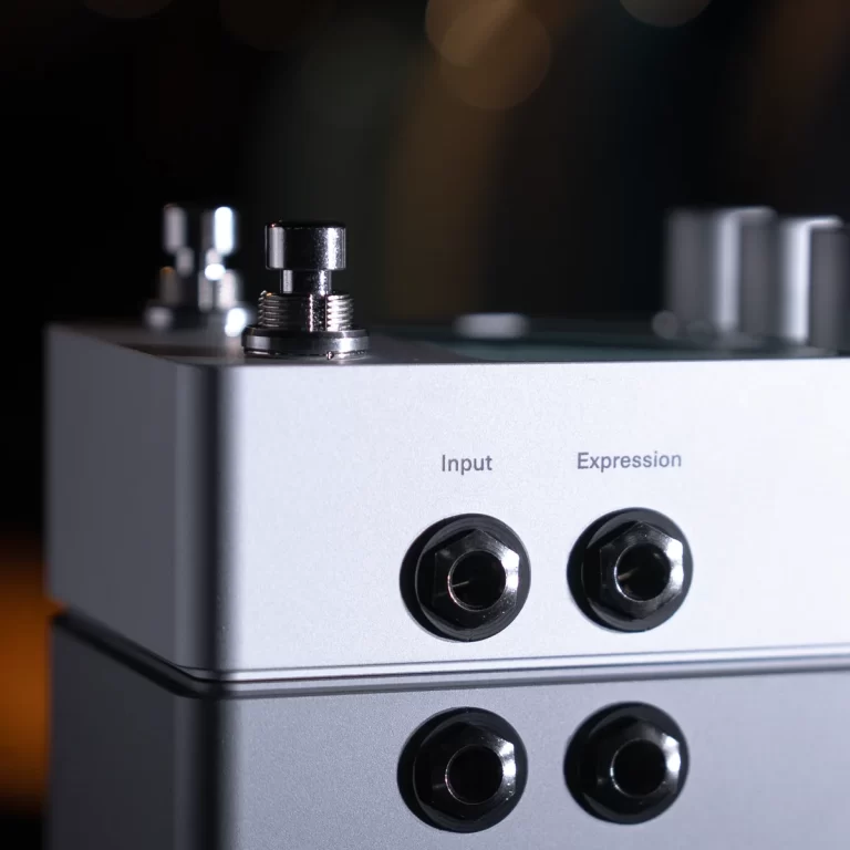 Close-up of a silver audio device showing input and expression jacks with a chrome knob on top, shallow depth of field behind. ขายราคาพิเศษ