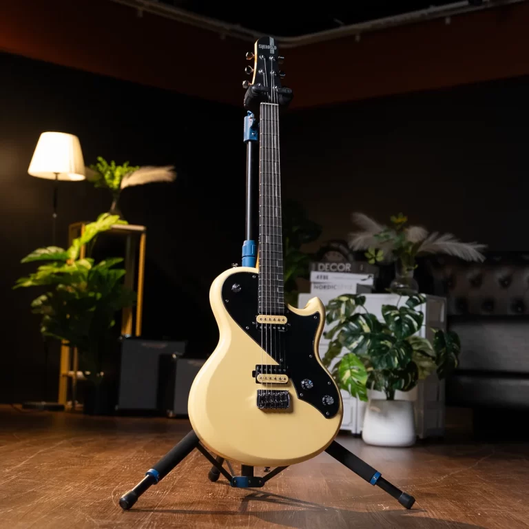 Cream-colored electric guitar with a black pickguard on a stand in a dim studio, with a lamp and plants in the background. ขายราคาพิเศษ