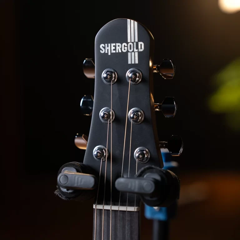 Close-up of a Shergold guitar headstock with six chrome tuning pegs and strings against a dark background. ขายราคาพิเศษ