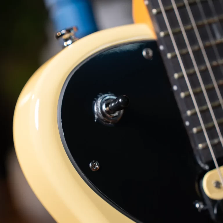 Close-up of a cream guitar body with a black pickguard and a chrome toggle switch by the neck area. ขายราคาพิเศษ