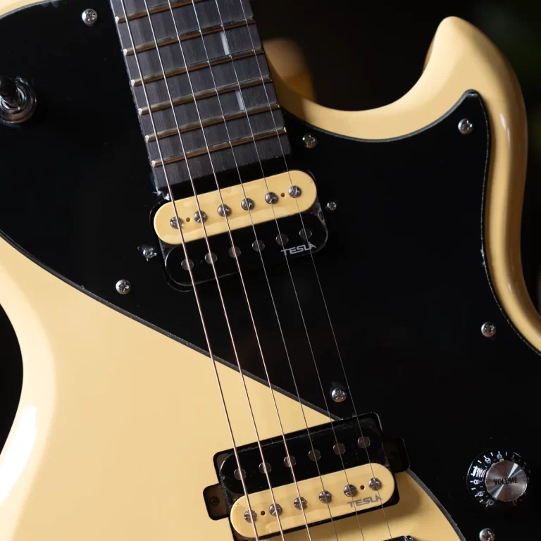 Close-up of a cream-colored electric guitar with a black pickguard, two cream Tesla pickups, and six strings visible across the fretboard nearby. ขายราคาพิเศษ