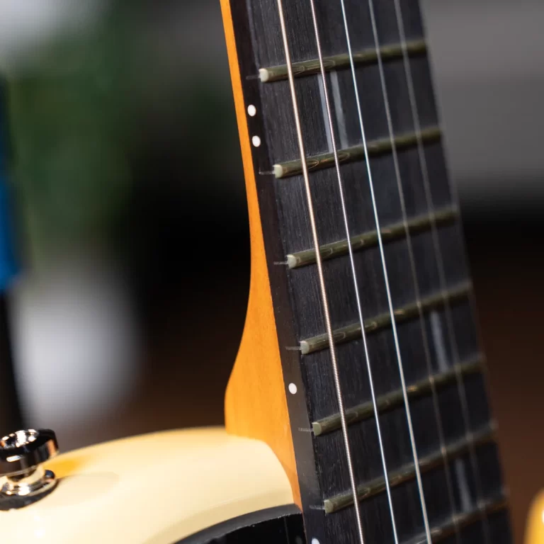 Close-up of a guitar neck with six strings and frets on a dark fretboard and an orange edge. ขายราคาพิเศษ