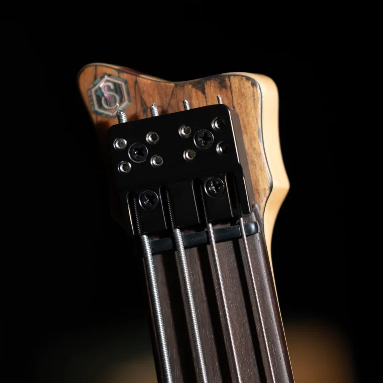 Close-up of a wooden guitar headstock with four metal strings and chrome tuning pegs against a dark background. ขายราคาพิเศษ
