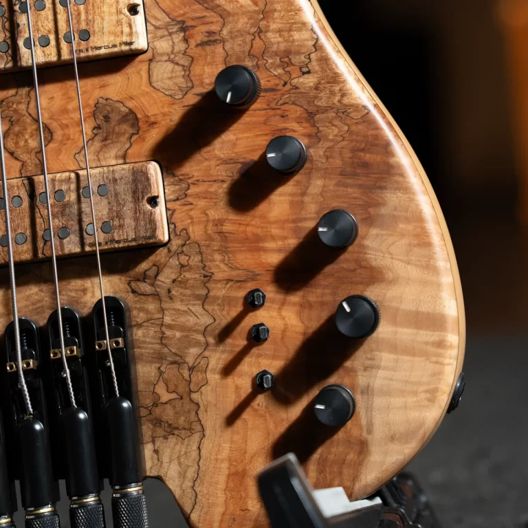Close-up of a wood-grain electric bass guitar body with black knobs and strings visible across the pickups and bridge area. ขายราคาพิเศษ