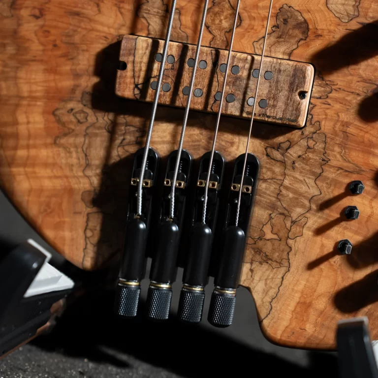 Close-up of a wooden guitar body with four strings, bridge saddles, and pickups in a detail shot. ขายราคาพิเศษ