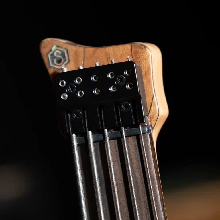 Close-up of a guitar headstock with six tuning pegs and wound strings against a dark background, showing the wood grain and hardware details. ขายราคาพิเศษ