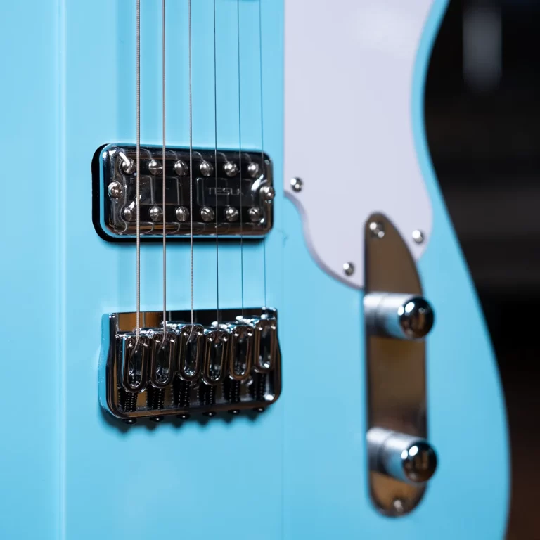 Close-up of a turquoise electric guitar bridge: chrome tremolo tailpiece, six strings, and a white pickguard visible nearby. ขายราคาพิเศษ