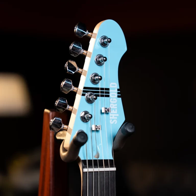 Close-up of a light-blue guitar headstock with six chrome tuners and strings, branding reading SHERGOLD on a dark background ขายราคาพิเศษ
