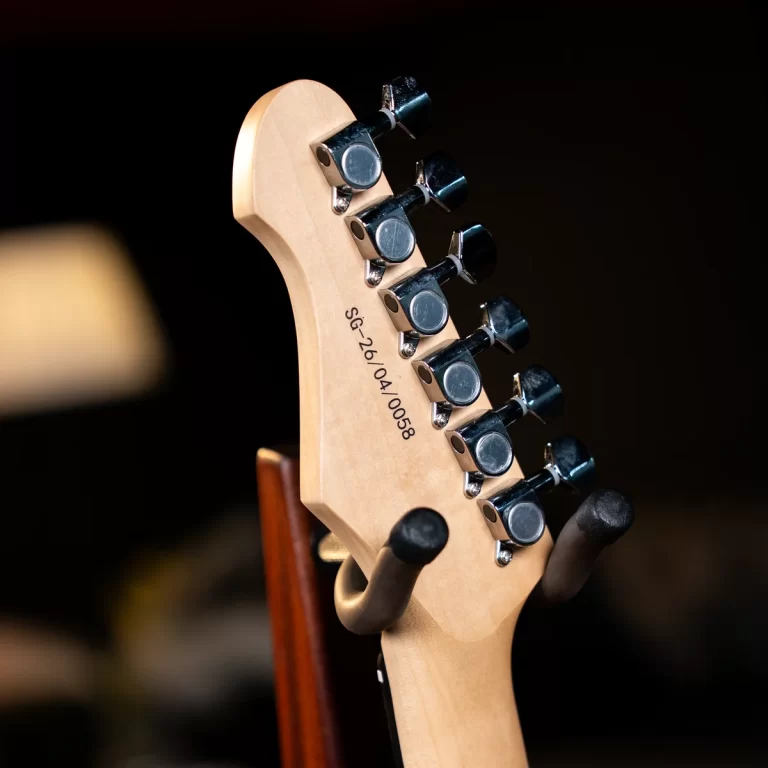 Close-up of a light wood guitar headstock with chrome tuning pegs, shallow depth of field, dark background behind. ขายราคาพิเศษ