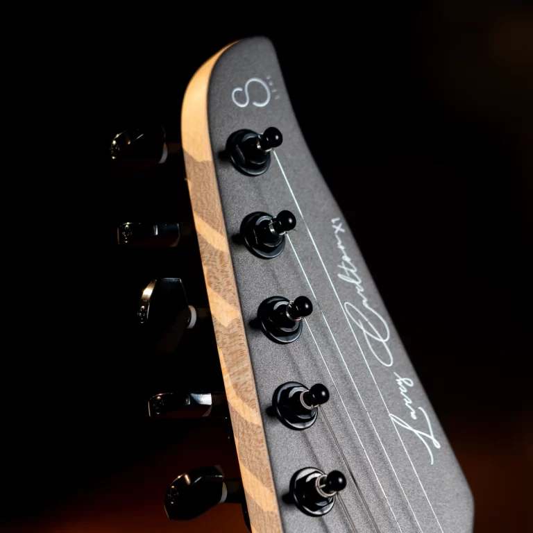 Close-up of guitar headstock with black tuning pegs and strings on a dark background. ขายราคาพิเศษ