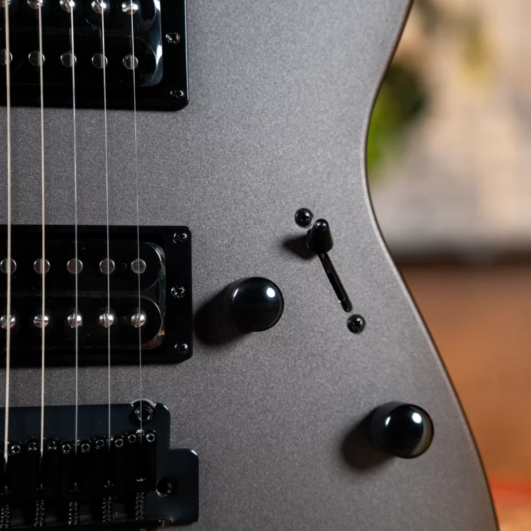 Close-up of a metallic gray electric guitar body, showing dual black humbucker pickups, metal strings, and control knobs. ขายราคาพิเศษ