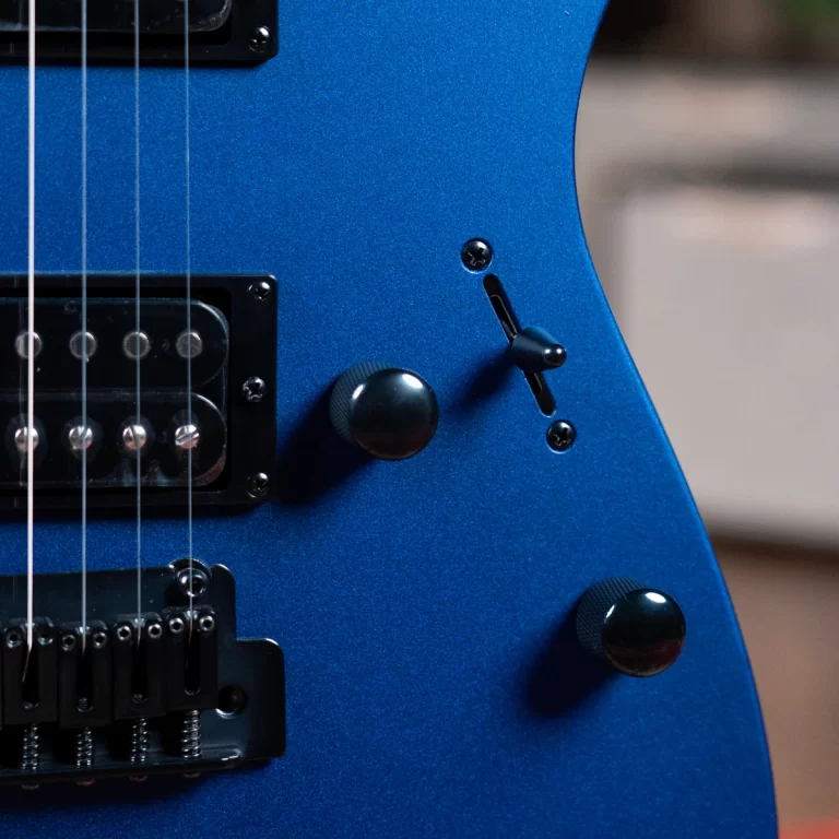 Close-up of a blue electric guitar body showing a bridge pickup, strings, and two black knobs with a small toggle switch nearby on the glossy blue finish. ขายราคาพิเศษ