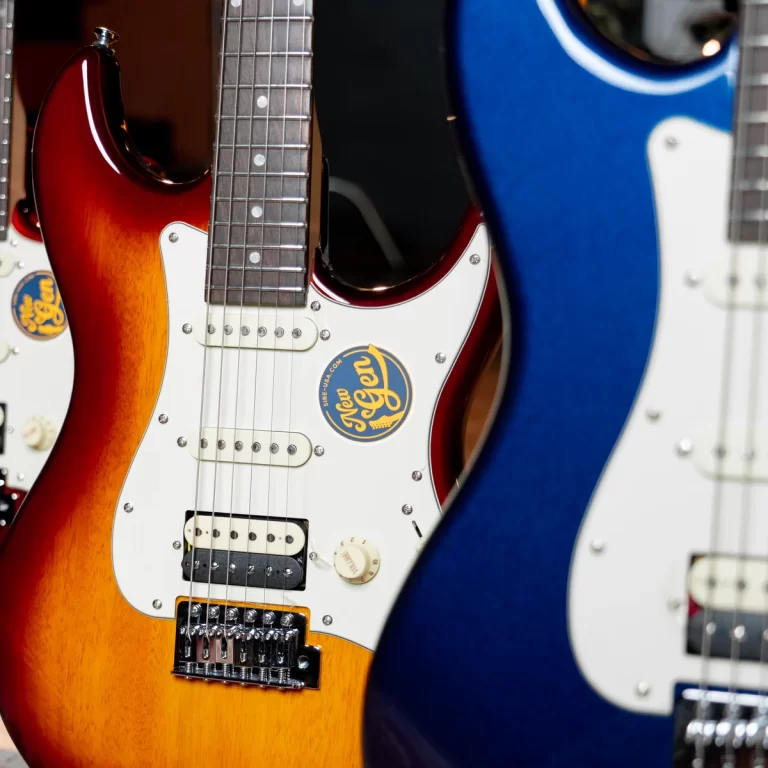 Close-up of a sunburst electric guitar with a white pickguard, three pickups, and chrome hardware among other guitars. ขายราคาพิเศษ