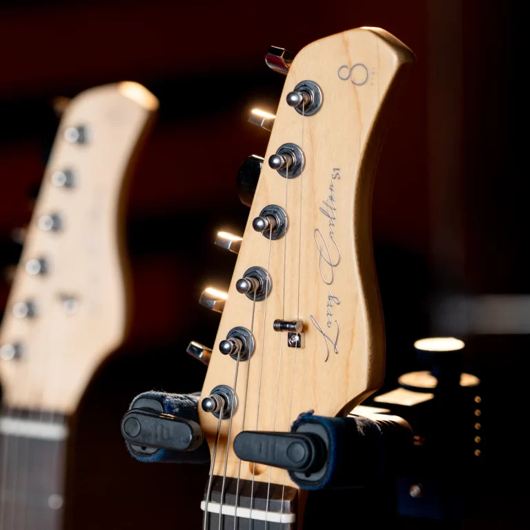 Close-up of a light wood electric guitar headstock with tuning pegs and a cursive logo. ขายราคาพิเศษ