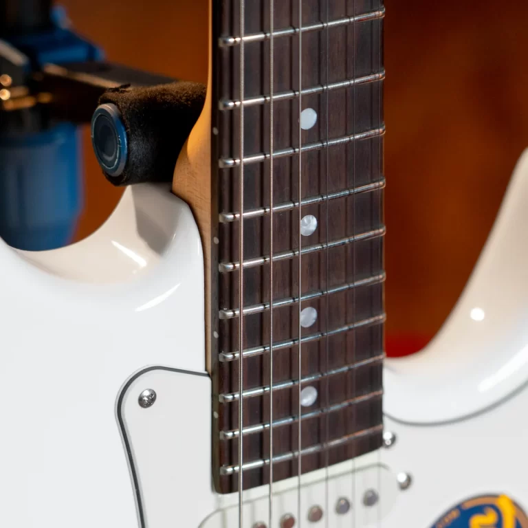 Close-up of a white electric guitar body and dark fretboard with metal frets and strings running along the neck. ขายราคาพิเศษ