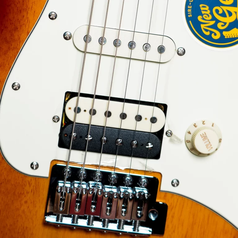Close-up of a white electric guitar body with two pickups, six strings, and a chrome bridge on an orange-toned edge. ขายราคาพิเศษ