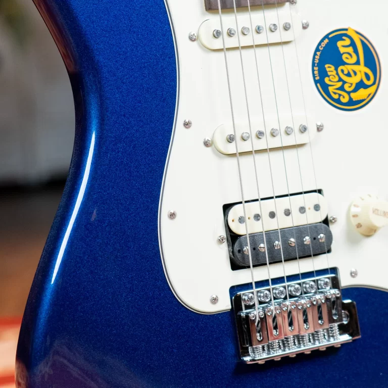 Close-up of a blue electric guitar body with a white pickguard, strings, pickups, and a round sticker on the body area. ขายราคาพิเศษ