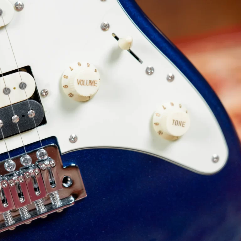 Close-up of a blue electric guitar showing white volume and tone knobs on the pickguard. ขายราคาพิเศษ