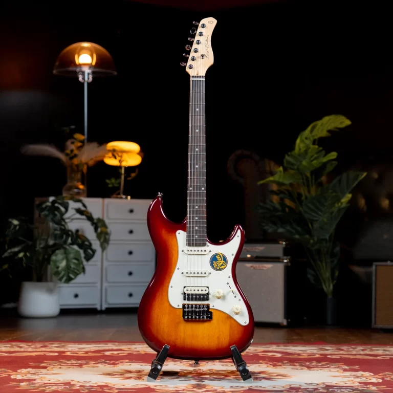 Sunburst Fender Stratocaster-style electric guitar on a stand in a warmly lit, plant-filled studio setting. ขายราคาพิเศษ
