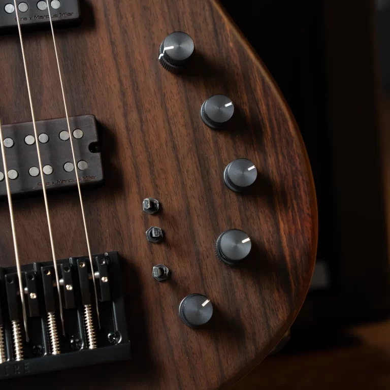 Close-up of a brown wooden electric bass guitar with four control knobs, a pickup, and strings visible across the body. ขายราคาพิเศษ