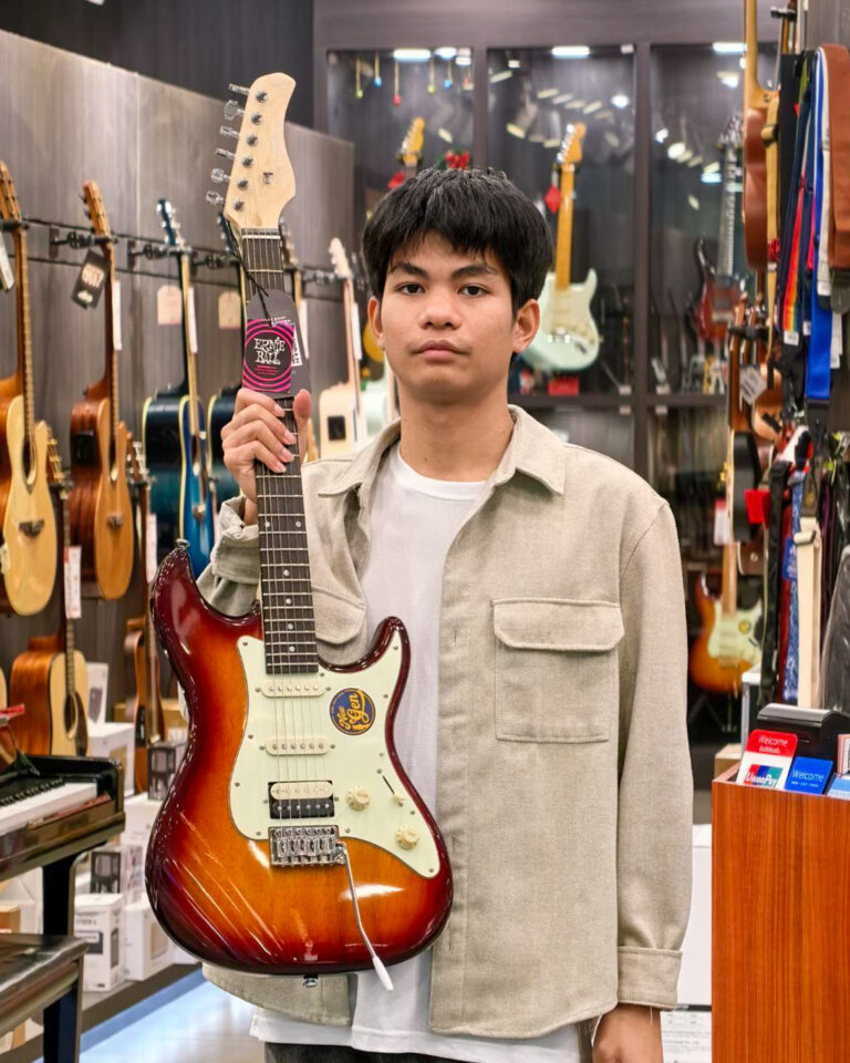 Young man in a music store holding a sunburst electric guitar.