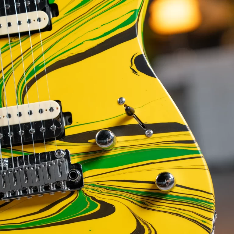 Close-up of a yellow electric guitar with green and black swirl patterns, showing pickups and chrome hardware. ขายราคาพิเศษ