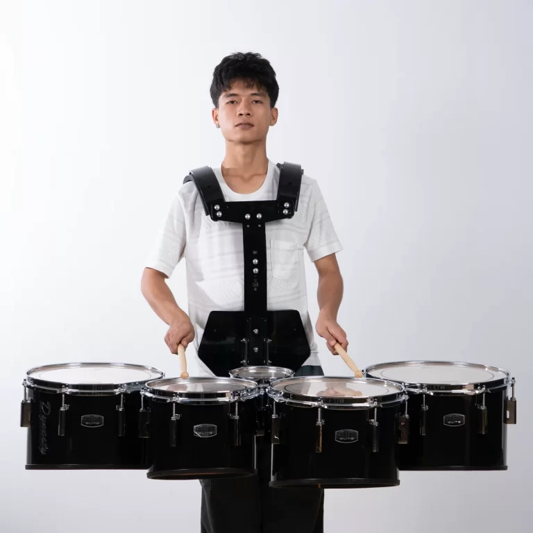 Young man wearing a black multiple-drum harness, standing behind five mounted drums with sticks, ready to play. ขายราคาพิเศษ