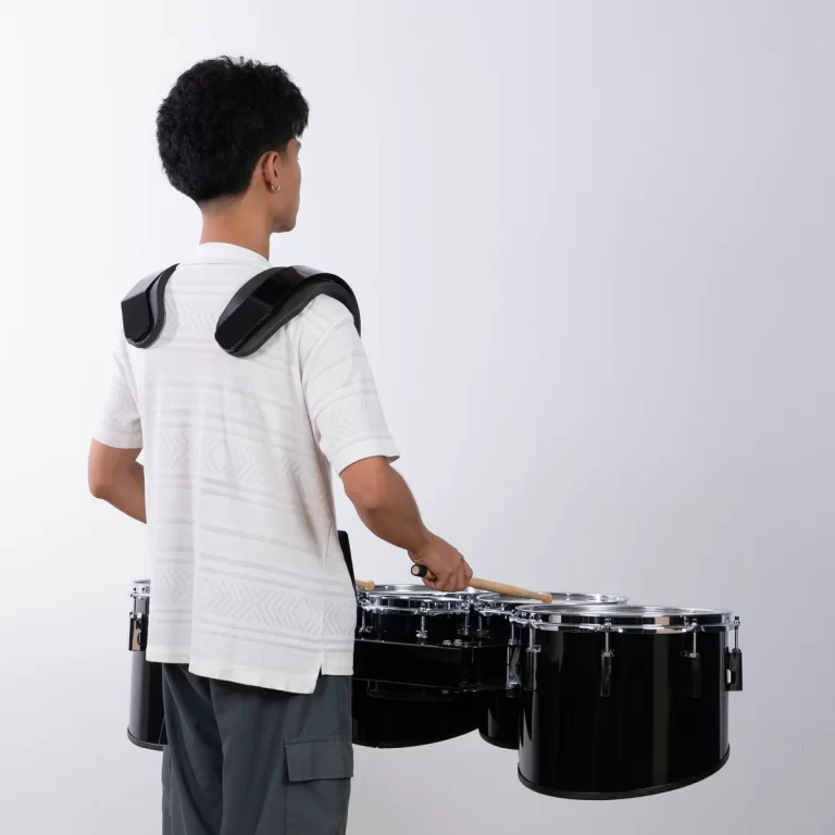 Person viewed from behind wearing a shoulder-mounted drum harness with three black drums, holding drumsticks ready to play. ขายราคาพิเศษ