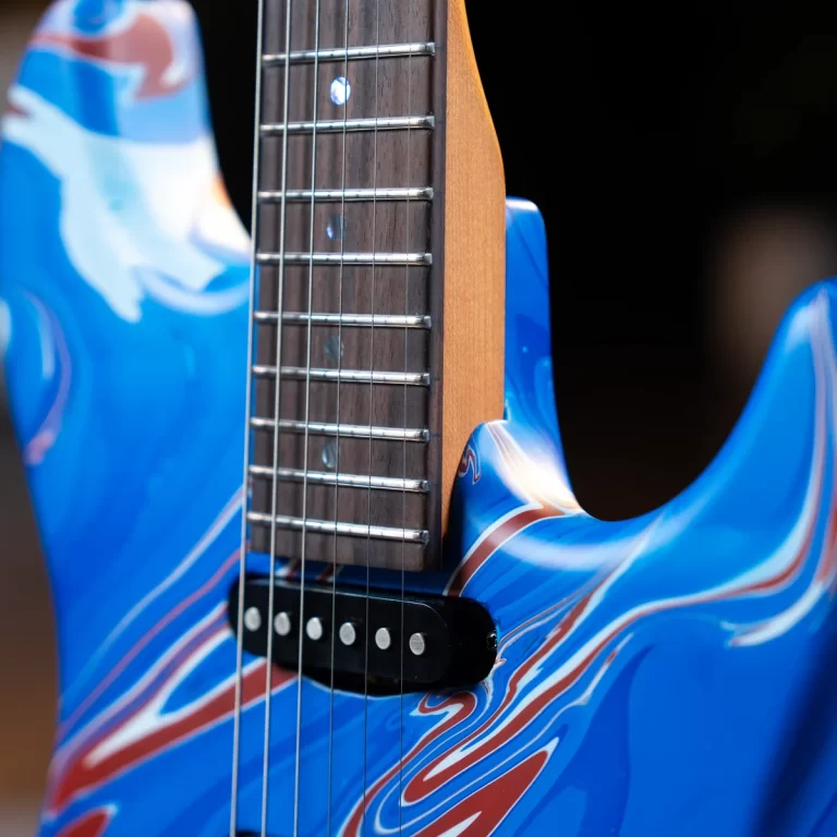 Close-up of a blue electric guitar with a wooden neck, metallic frets, and pickup detail showing swirling red-white patterns on the body. ขายราคาพิเศษ