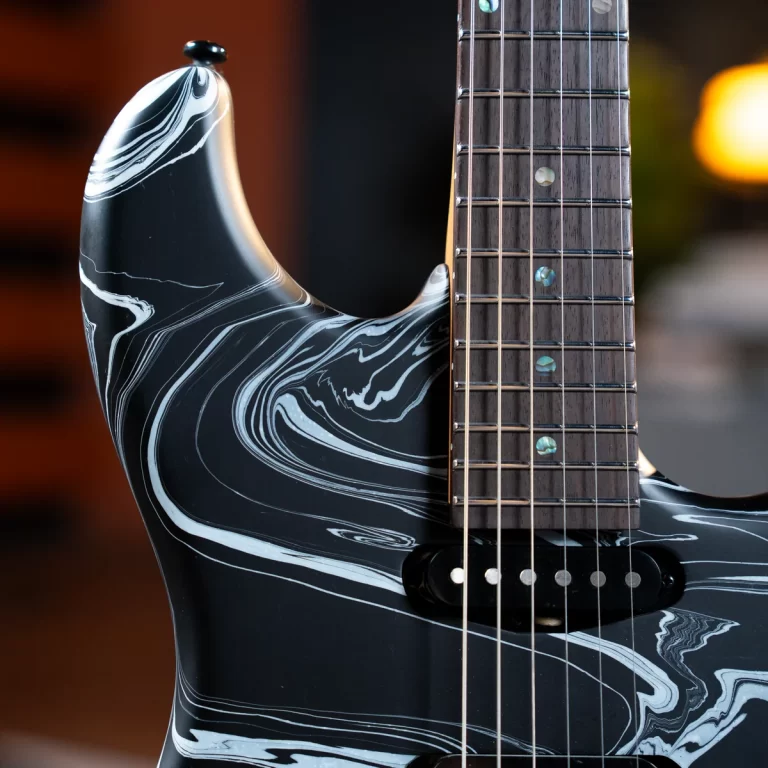 Close-up of a black electric guitar with a white marble pattern on the body and a dark fretboard with dot inlays.”, ขายราคาพิเศษ