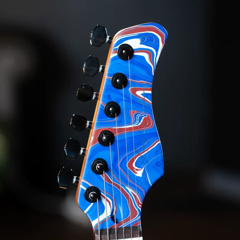 Close-up of a guitar headstock with a blue, red, and white marbled finish and six tuning pegs. ขายราคาพิเศษ