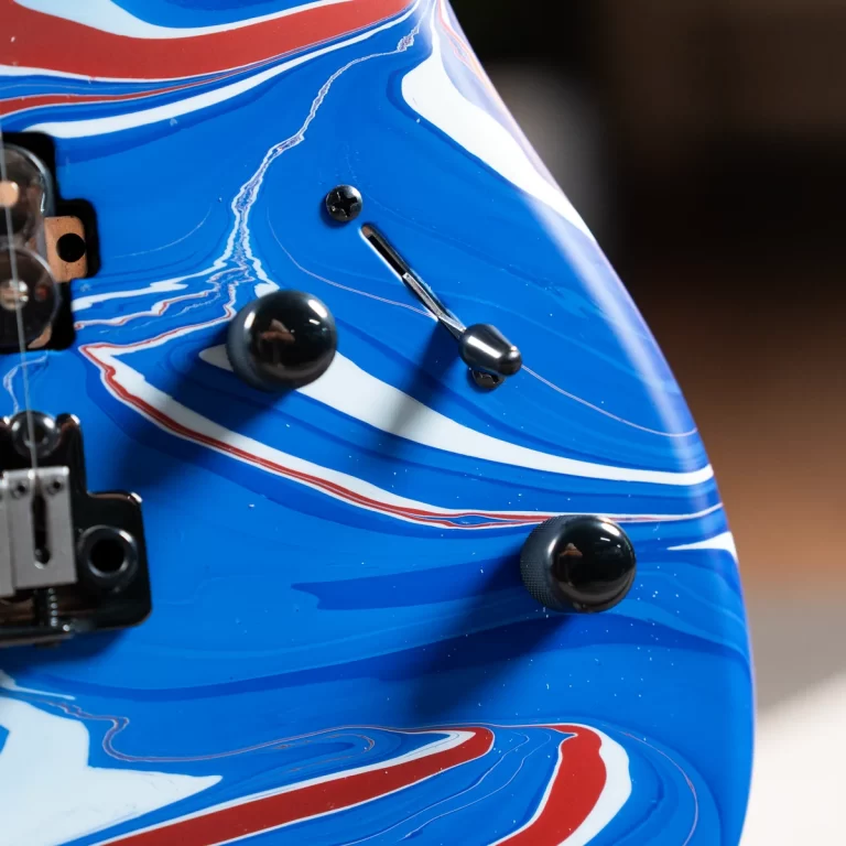 Close-up of a blue electric guitar body with black control knobs and a chrome tremolo arm, featuring red and white racing stripe accents. ขายราคาพิเศษ