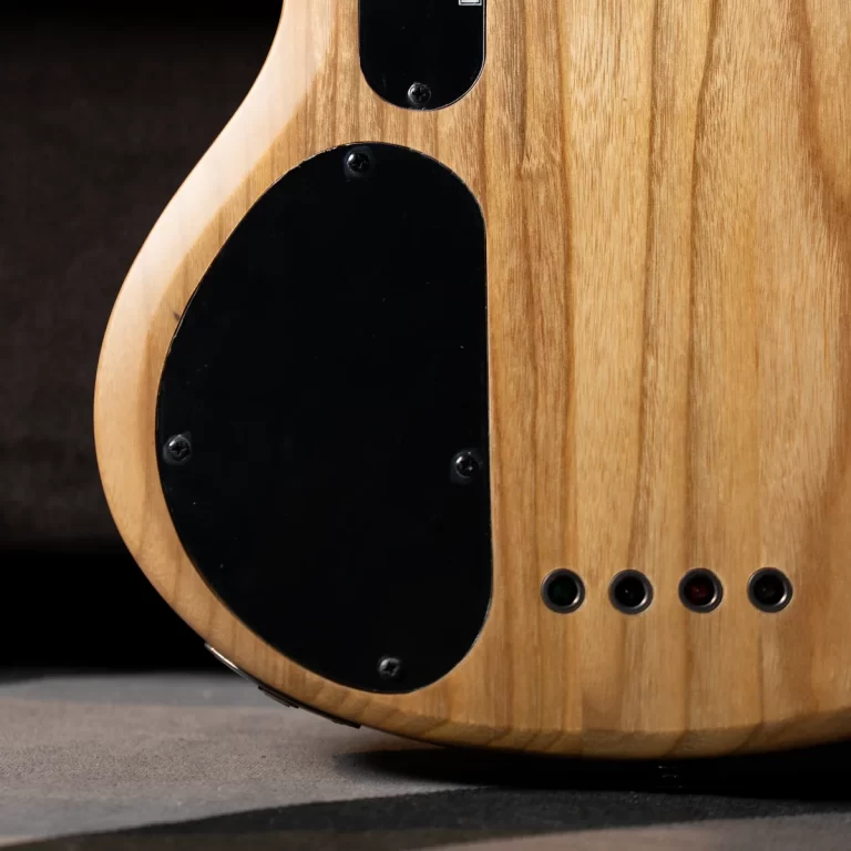 Back view of a natural-finish electric guitar showing wood grain, a large black rear cavity cover with screws, and a row of small circular ports at the bottom edge ขายราคาพิเศษ