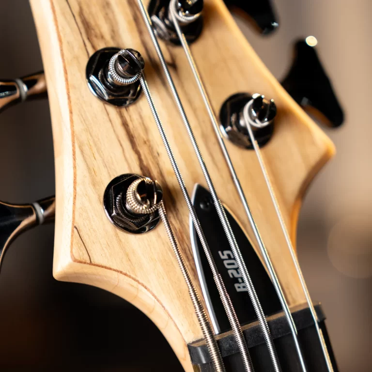 Close-up of a natural wood bass guitar headstock with four chrome tuning pegs and wound strings in view. ขายราคาพิเศษ