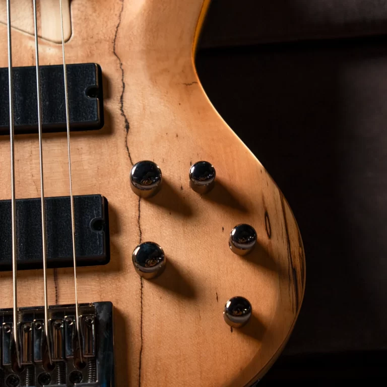 Close-up of a natural wood electric bass guitar body with four chrome knobs and two black pickups. ขายราคาพิเศษ