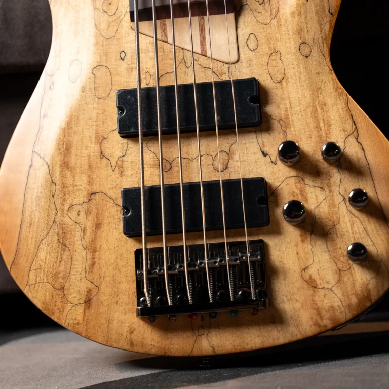 Close-up of a worn light-wood electric bass guitar body with two black pickups, strings, and a metal bridge. ขายราคาพิเศษ