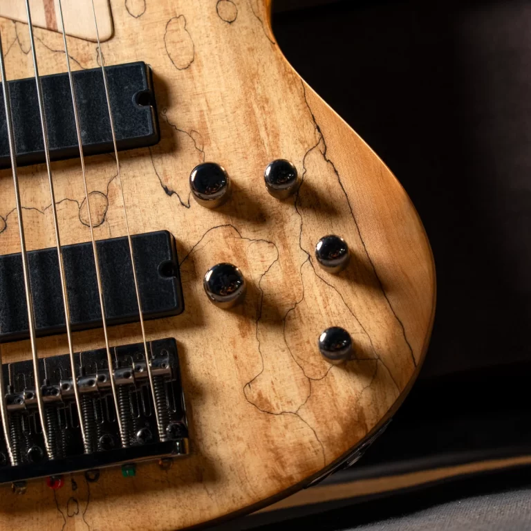 Close-up of a worn natural-finish bass guitar with four strings, two pickups, and four control knobs on a cracked wooden body. ขายราคาพิเศษ