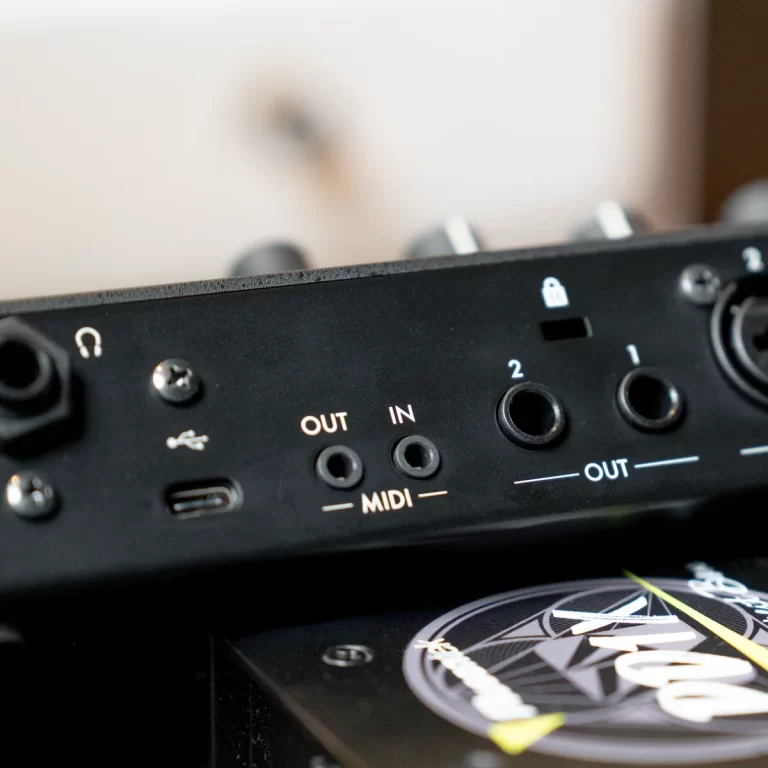 Close-up of a black audio interface panel showing MIDI OUT/IN jacks, a USB port, and labeled inputs, with a decorative circular graphic in the foreground ขายราคาพิเศษ