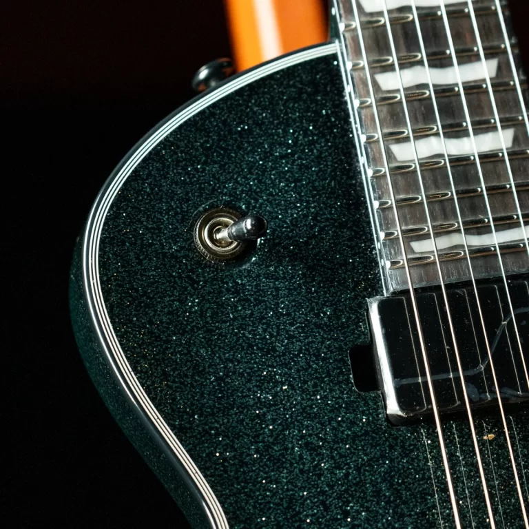 Close-up of a glittery dark-green electric guitar body with a metal toggle switch and strings running along the right side. ขายราคาพิเศษ