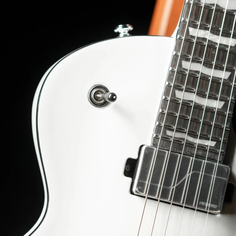 Close-up of a white electric guitar body with a chrome toggle switch and pickup against a black background. ขายราคาพิเศษ