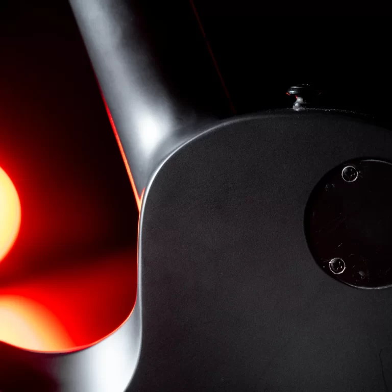Close-up of a black electric guitar body with part of the neck and a red glow in the left background, highlighting the edge of the instrument against a dark backdrop. ขายราคาพิเศษ